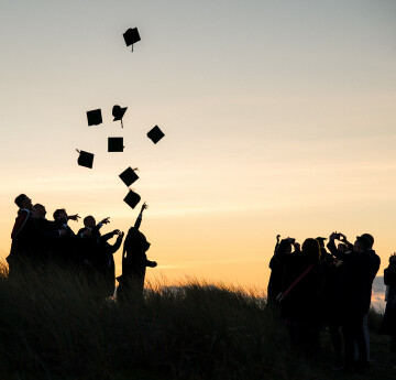 Students throwing hats in the air against a sunset background.