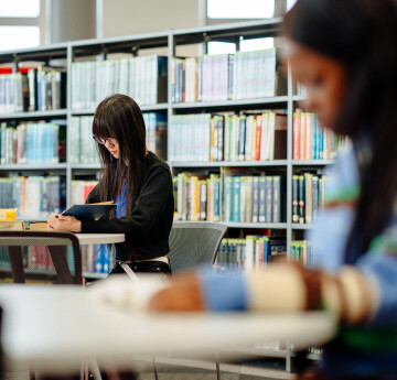 two students in front of a library stack filled with books