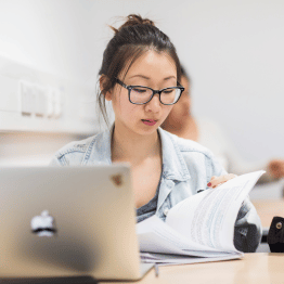 Student revising at a desk with a laptop and papers.