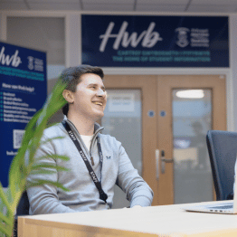 Staff member laughing and sitting down at the Hwb front desk.