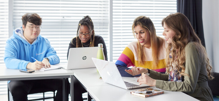  Group of students sitting at a table looking at laptops 