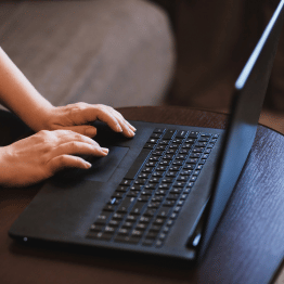 Laptop on a desk, with hands typing on the keyboard.