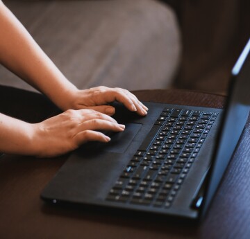 Close up of a laptop on a table, with two hands visibly typing